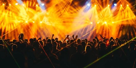 Publikum bei einem Konzert. Über der feiernden Menge leuchten gelbe Lichteffekte.  gelbe 