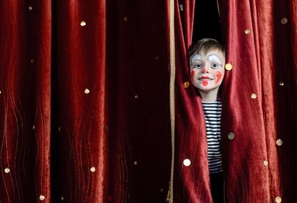 Child made up as a clown, behind a red curtain 
