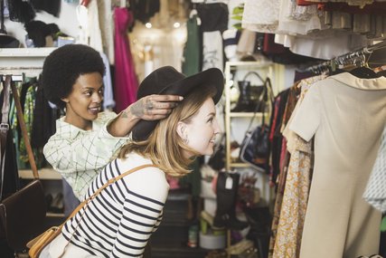 Ladenbesitzerin probiert Hut auf Kundin in Vintage Boutique