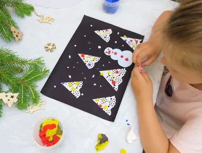 Young girl makes Christmas card with snowman and Christmas tree from bird's eye view